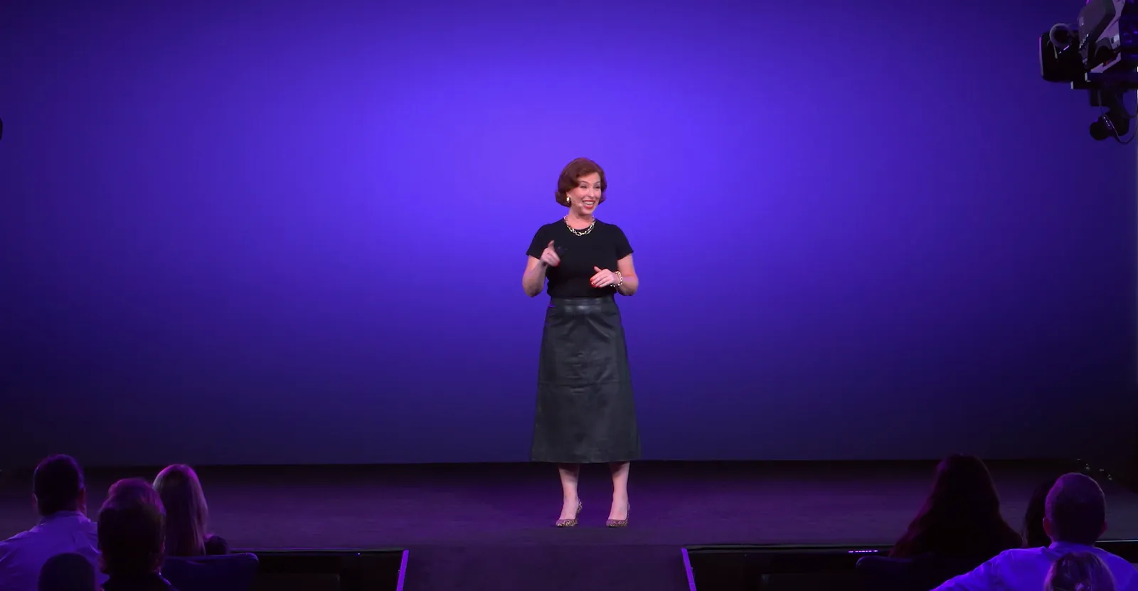 A keynote speaker alone on a deep blue stage in front of a seated audience
