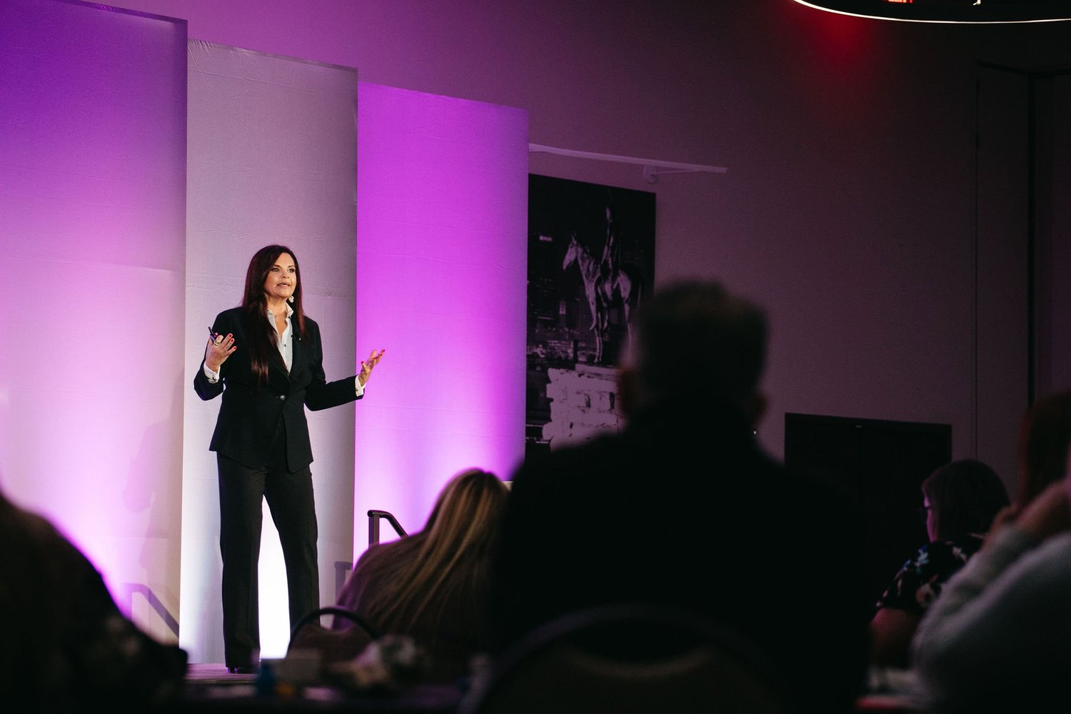 Violet Rainwater speaking on a purple-lit stage to a seated audience